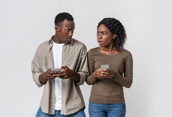 Annoyed black couple with smartphones looking at each other