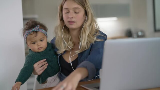 Young woman teleworking from home and watching baby girl 