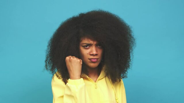 Young african american curly woman showing fist to camera, aggressive facial expression