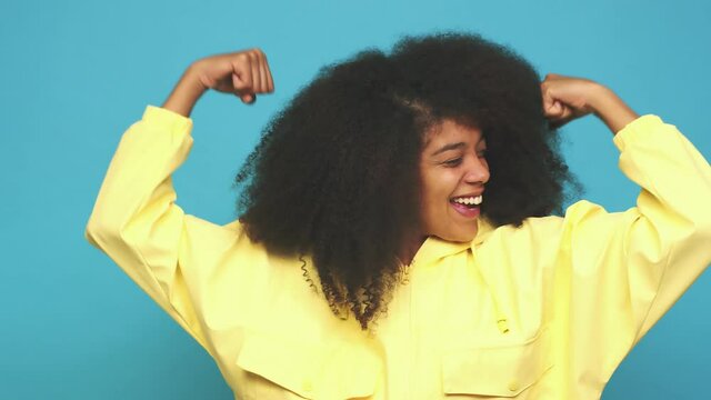 Young african american curly woman showing strength gesture with arms, symbol of feminine power