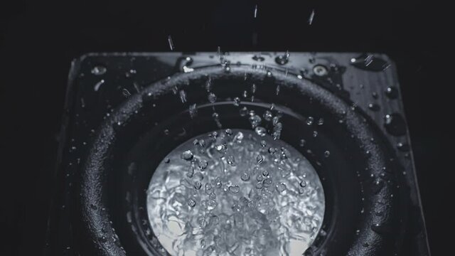 Dark Wave Audio and Black Water Liquid on a Plate. Subwoofer speaker with water. Droplets explode over the sound of the bass. Liquid jumps on the audio speaker. Background for a party. Slow motion.