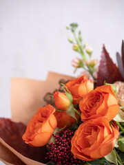 A bouquet of fresh flowers of spray roses of coral color and beige dianthus in craft paper on a light background