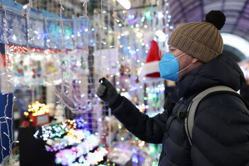 Man with protective face mask and warm clothes choosing Christmas garland in market