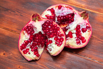 The pomegranate, broken into two parts, lies on a wooden background