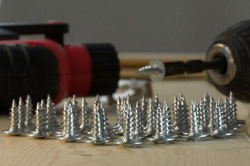 Cordless drill and screws. Electric drill with drill bits, screws on wooden background. Bunch of screws on wood planks. Assorted tools. Handyman professional DIY project workplace tabletop. 