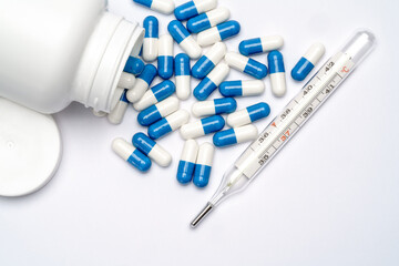 Medications capsules in a bottle and thermometer on light grey background