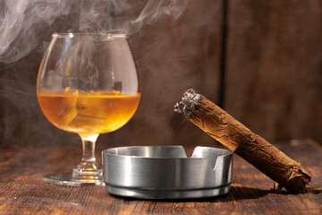 Glass of whisky and lighted cigar in an ash tray
