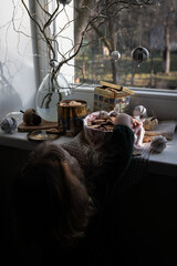 Three metal boxes with homemade Swedish pepparkakor (pepper cookies) and gingerbread cookies and willow branches decorated with Christmas ornaments on the windowsill. 