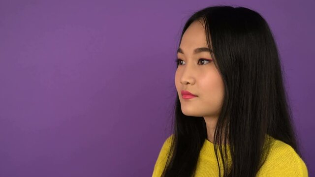 three-quarter portrait of a young woman. calm emotions. Asian woman on purple isolated background. 4K