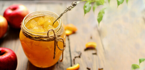 Apple jam in a transparent glass jar. Jam from apples and orange on a light background. Delicious marmalade.