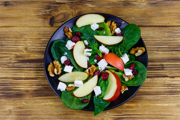 Autumn spinach salad with apple, feta cheese, walnut and dried cranberry on wooden table. Top view. Healthy vegetarian food