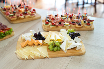 The buffet at the reception. Assortment of canapes on wooden board. Banquet service. Catering, snacks with different types of cheese and meat. Party Concept.
