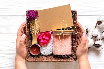 Female hand holds care box Set of eco - friendly cosmetics Bath salt, wooden comb, pumice stone, aroma candles, handmade soap, washing sponge on wooden background Gift for girlfriend, mother Top view - 397796795