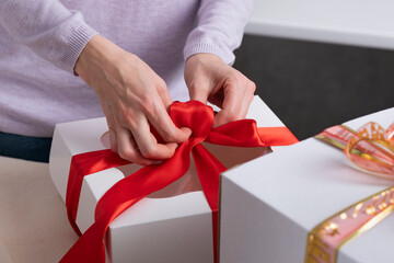 Woman is packing gifts. White box with red ribbon.