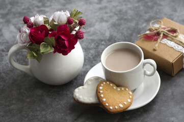 Obraz na płótnie Canvas jug with red and pink roses, sprigs of eucalyptus, a cup of coffee with milk, heart-shaped cookies, gift box on a dark gray background. congratulations on Valentine's Day, Mother's Day.