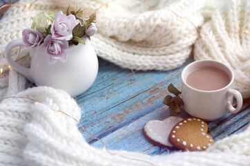 Obraz na płótnie Canvas a white knitted scarf, a jug with little pink roses, a cup of coffee with milk and heart-shaped cookies. greeting card Happy Valentine's Day, Mother's Day.