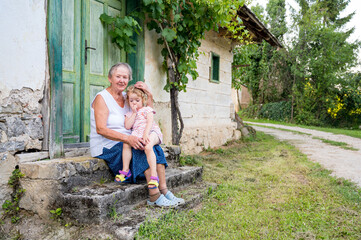 Grandmother sitting with her grandmother in front of her old house.