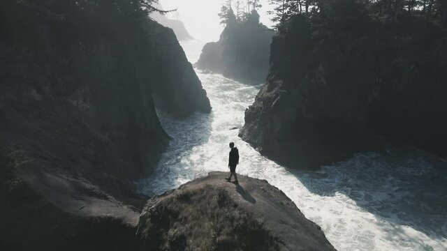 Rearview of a man walking towards the end of the rocky cliff with spectacular mighty ocean view.
