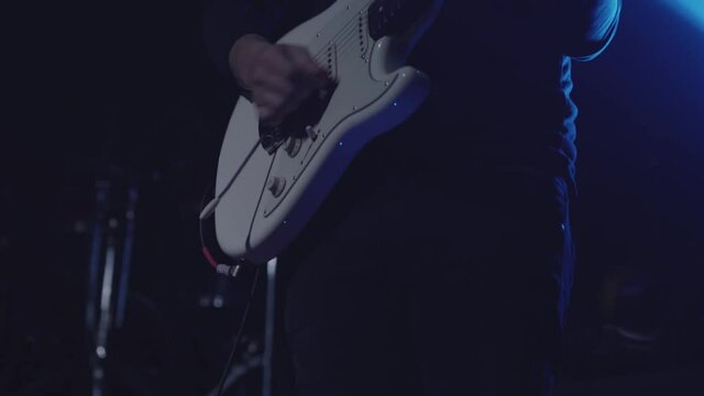 Close-up shot of a man's hand playing an electric guitar on stage. Six-string guitar. The guitarist in black performs on stage, rock music concert. 