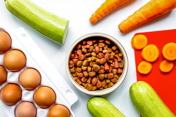 dry food for dogs, eggs and vegetables on kitchen background top view