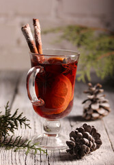 Alcoholic beverage. Mulled wine. Cocktail of red wine, apple, orange, lemon, cloves and cinnamon in a clear glass on a light wooden table with fir and cone. Christmas. Background image, copy space