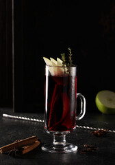 Alcoholic beverage. Mulled wine. Cocktail of red wine, apple, orange, lemon, cloves and cinnamon in a clear glass on a black table.  Bar menu. Background image, copy space, vertical