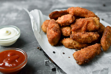 Homemade chicken nuggets. Nuggets on white parchment. Ketchup and mayonnaise. Copyspace. Gray background.
