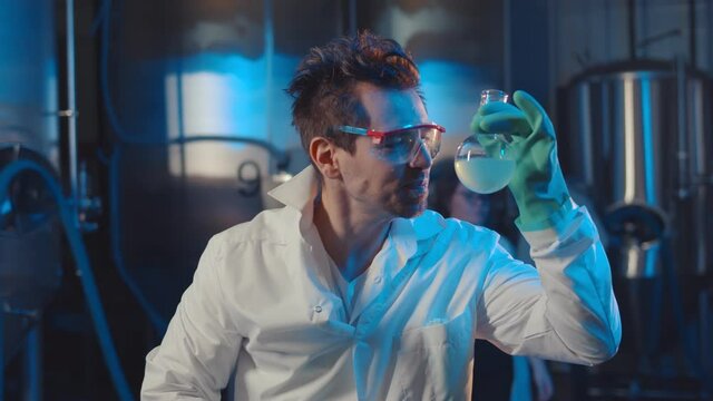 Mad scientist drinking blue liquid from glass flask in industrial lab