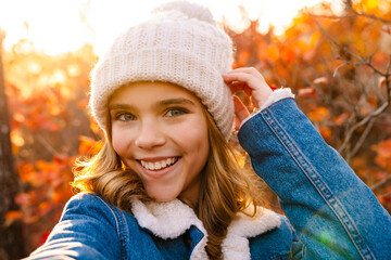 Happy girl walking outdoors in autumn park taking a selfie
