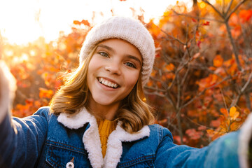 Happy girl walking outdoors in autumn park taking a selfie