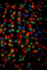 Multicolored bokeh on a black background. Multicolored lights from the Christmas garland. Good New Year spirit. Blurred focus.
