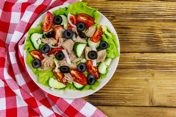 Tasty tuna salad with lettuce, black olives and fresh vegetables on wooden table. Top view