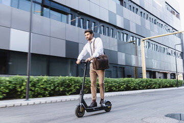 bearded businessman in formal wear riding electric scooter and holding bag near building © LIGHTFIELD STUDIOS
