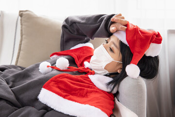 Sick Xmas woman in Santa clause suit having headache wearing face mask due to coronavirus and COVID-19 outbreak in Christmas period, concept of Covid Christmas or new normal social distancing Xmas