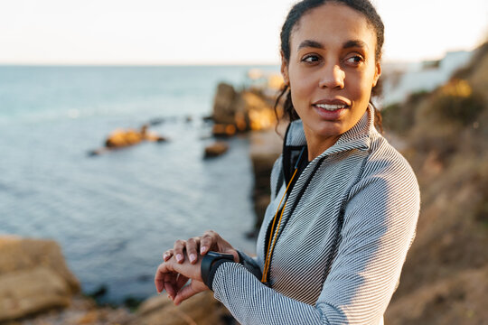Focused african american sportswoman looking at smartwatch at beach - Powered by Adobe