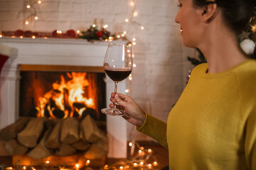 Back view of woman drinking wine from glass sitting and relaxation near fireplace and christmas tree.