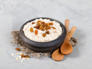 Multi cereal milk porridge with raisins in a wooden bowl on a linen napkin on a light background in rustic style