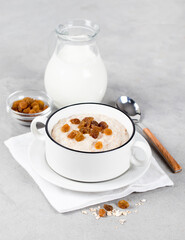 Multi cereal porridge with raisins and milk in a bowl on a light gray background