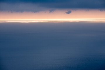 Fototapeta na wymiar surface de mer bleu gris avec une ligne horizontale de lumière à l'horizon sous des nuages gris bleus 