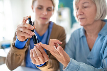 Caregiver or healthcare worker with senior woman patient, measuring blood glucose indoors.