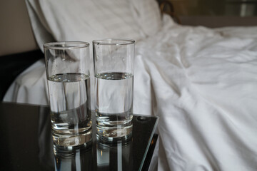 Two glass of water on the table beside the bed