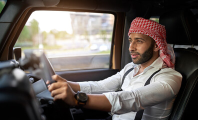 Arab businessman driving car wearing traditional headscarf keffiyeh