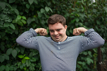 Portrait of down syndrome adult man standing outdoors at green background, flexing muscles.
