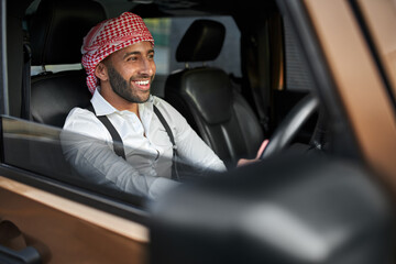 Smiling arab businessman driving car wearing traditional headscarf keffiyeh