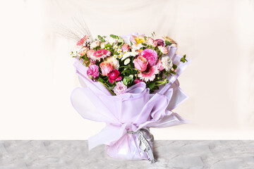 A bouquet of flowers kept on a marble against a plain cream background.