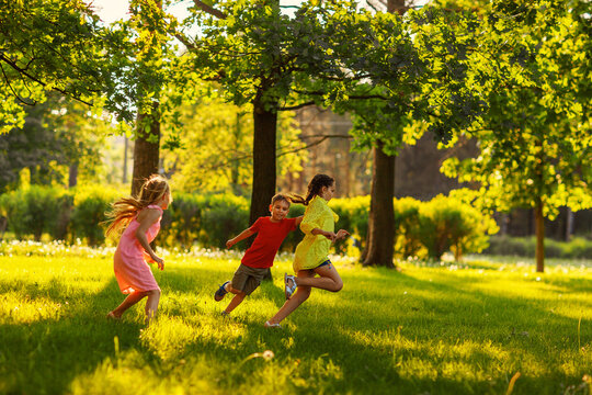 Group of three children having fun playing tag game in sunny summer park. Little friends running on green grass, chasing each other and trying to touch