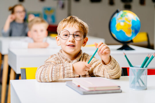 Cute male student in eyeglasses in class with globe in elementary school.