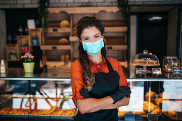 Fototapeta na wymiar Beautiful young female worker with protective mask on face working in bakery.