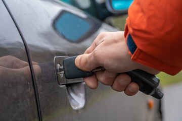 Close-up of a man's right hand in an orange jacket inserting a key into the car door lock.