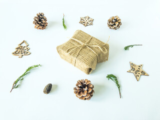 Arrangement of wooden christmas ornaments, pine cones and pine branches with a christmas present box in the middle on an isolated white surface, top view